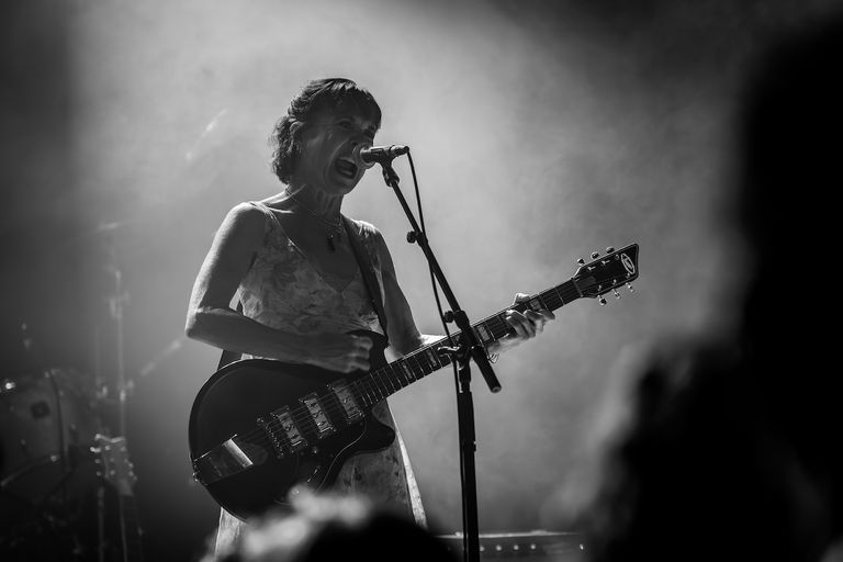 Black and white live performance photograph of Kristin Hersh singing into a microphone and playing an electric guitar, shot by Rob Mezzatesta.
